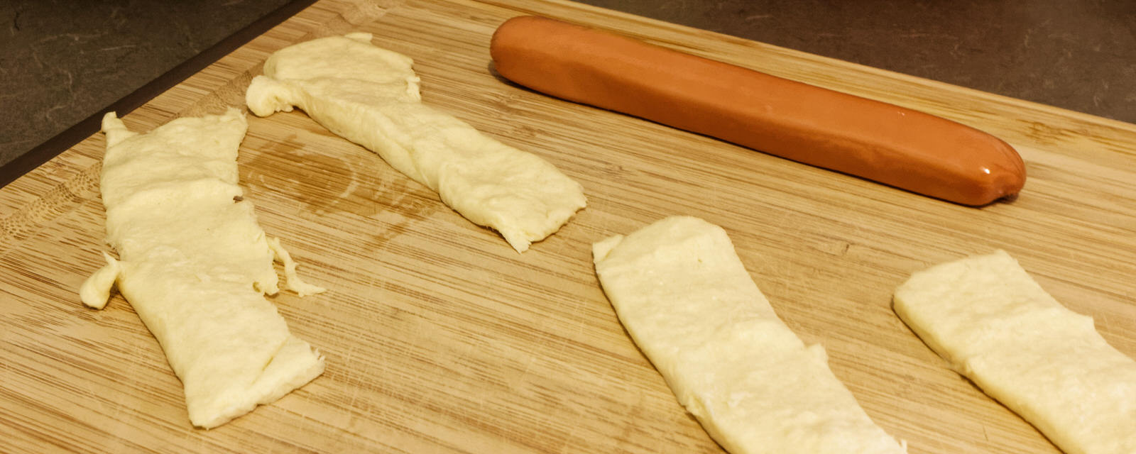 Pillsbury Crescent stripes on a cutting board with a wiener sausage